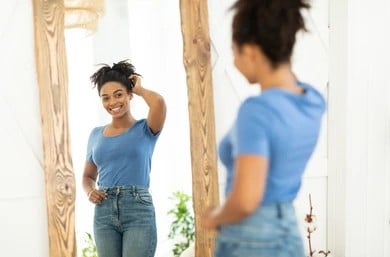 Woman is happy with her own weight loss progress as she looks in a full-body mirror.