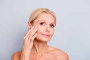 A woman smiling with her hand on her cheek after a laser skin tightening procedure